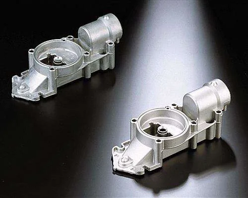 The image shows a pair of aluminum die casting parts on a black surface. The parts are silver in color and have a glossy finish. They are arranged in a symmetrical pattern, with each part slightly ove