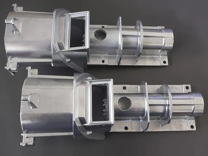The image shows a pair of metal parts on a gray surface, which appear to be part of a high-quality aluminum die casting machine. The metal parts are silver in color and have a glossy finish.
