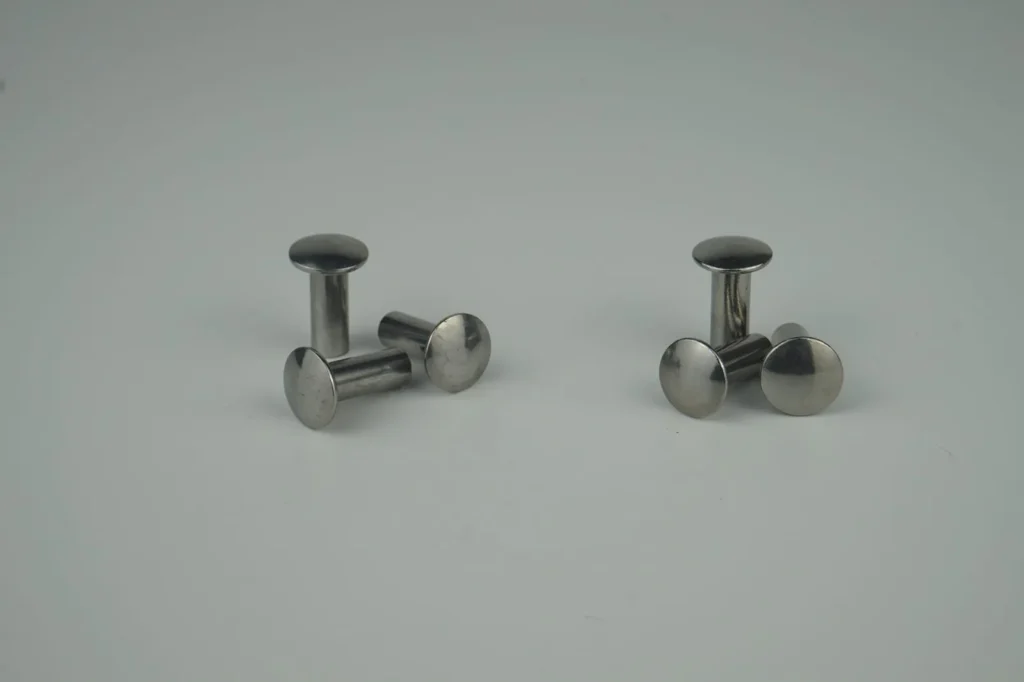 The image shows a pair of stainless steel stud earrings on a white surface. The earrings have a sleek, metallic finish and are arranged in a symmetrical pattern. The background is a bright white, high