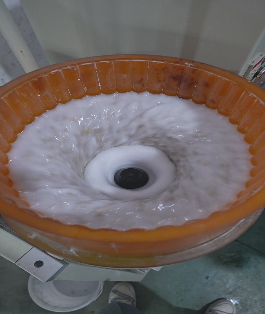 Inside of a running bowl finishing machine: orange polyurethane lining, water and media moving in a toroidal flow around the centre hub