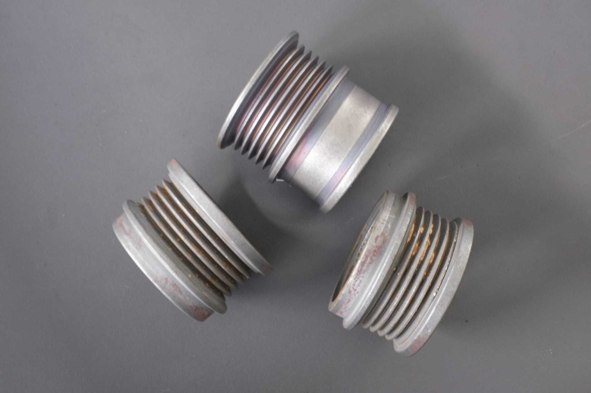 Three threaded metal fittings before finishing, with rust and oxide in the thread crests and groove walls