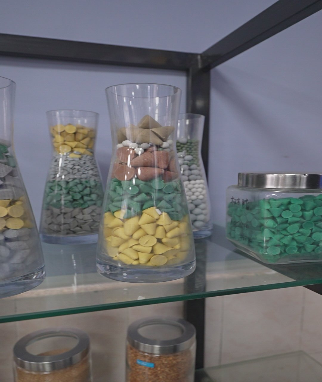 Clear jars of media samples in different colours and shapes: yellow cones, green triangles, brown and white cylinders